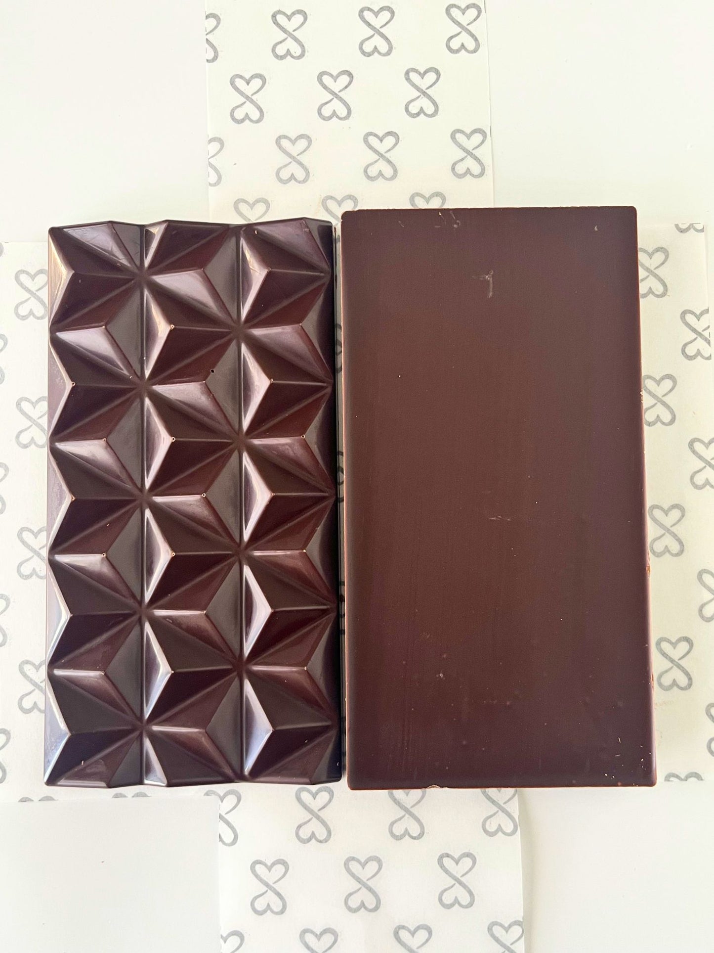 dark chocolate bar front and back. one side is smooth and the other shows geometric pyramid shapes