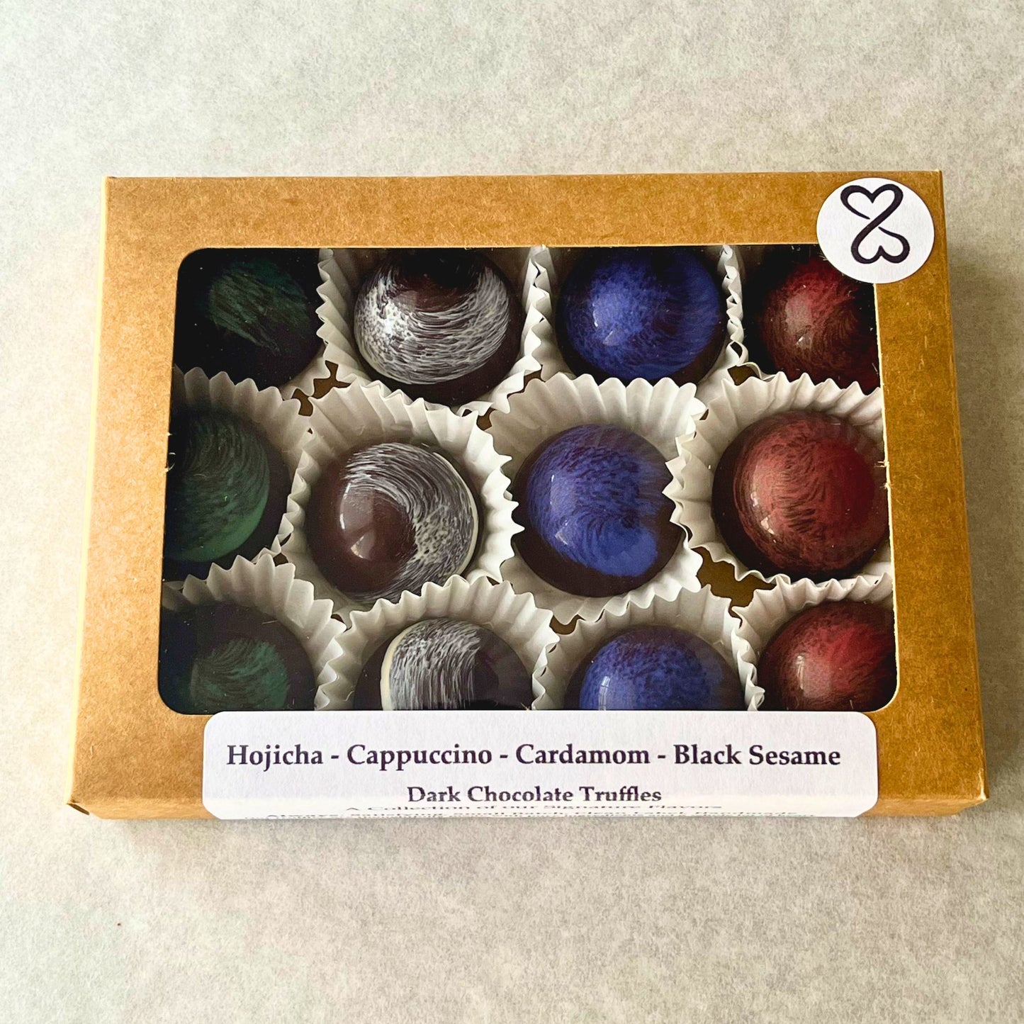 Box of dark chocolate truffles with colorful coatings on a beige background