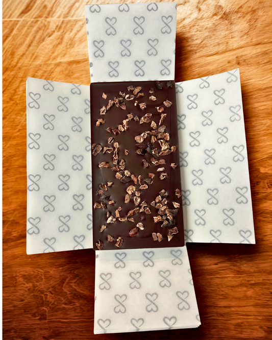 Chocolate bar with cacao nibs on patterned paper on a wooden surface
