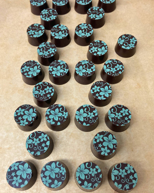 a collection of small circular chocolate truffles with a green floral pattern on the top