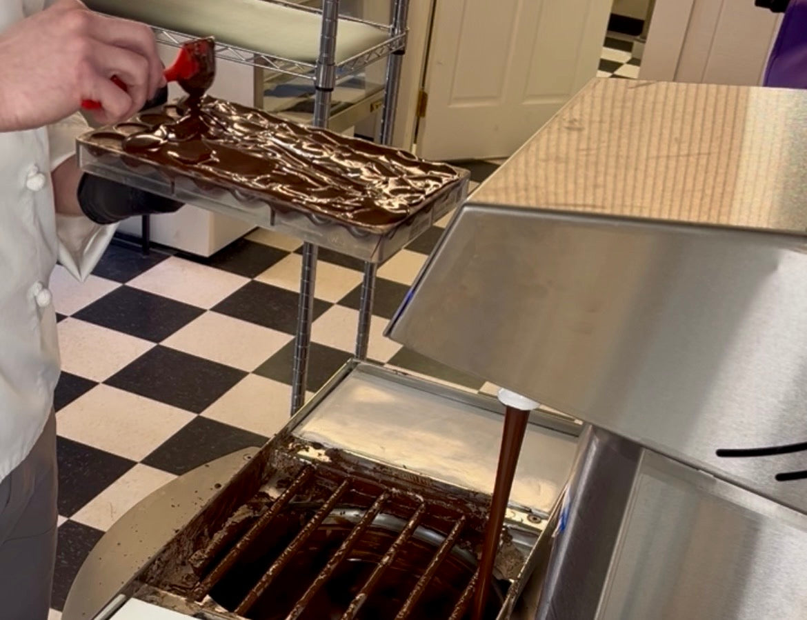 chocolatier spreading chocolate on a mold to seal chocolate truffles. 