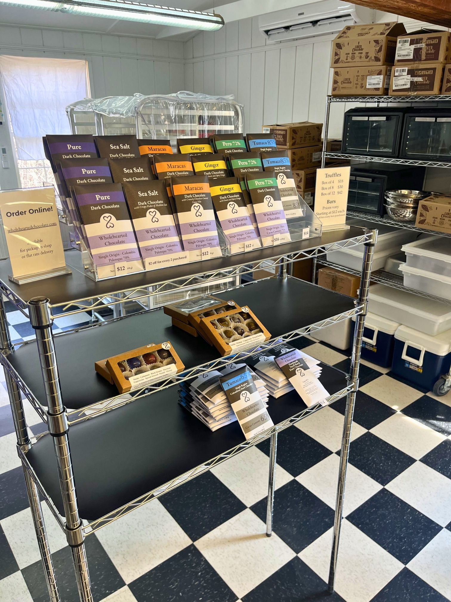 Display of chocolate bars and truffles on a metal rack in a store with checkered floor.