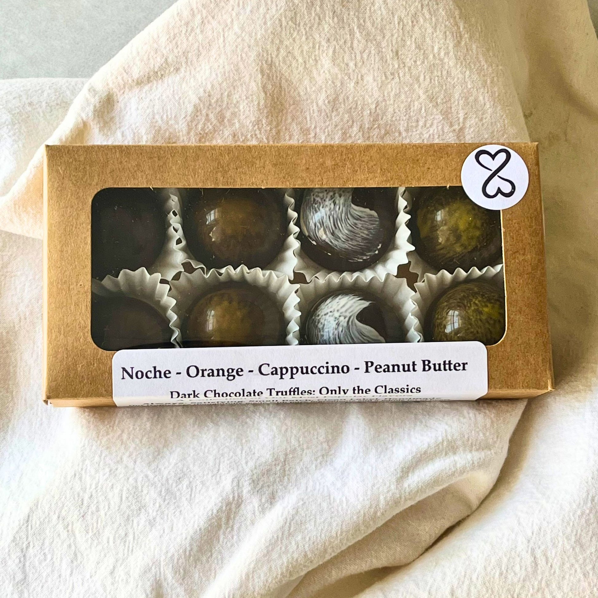 Box of dark chocolate truffles with visible flavors on a beige fabric background