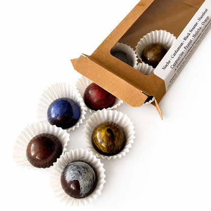 Assorted chocolates in white paper cups with an open box on a light gray surface