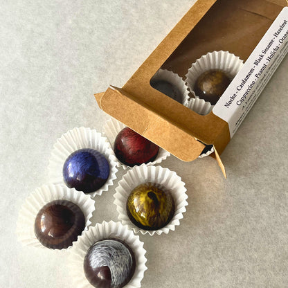 Assorted chocolates in white paper cups with an open box on a light gray surface