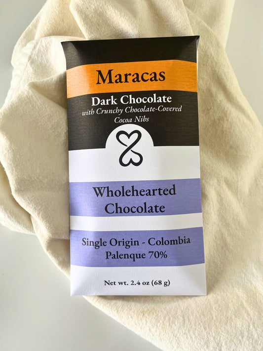 dark chocolate bar packaging titled Maracas. placed on a white linen fabric in background