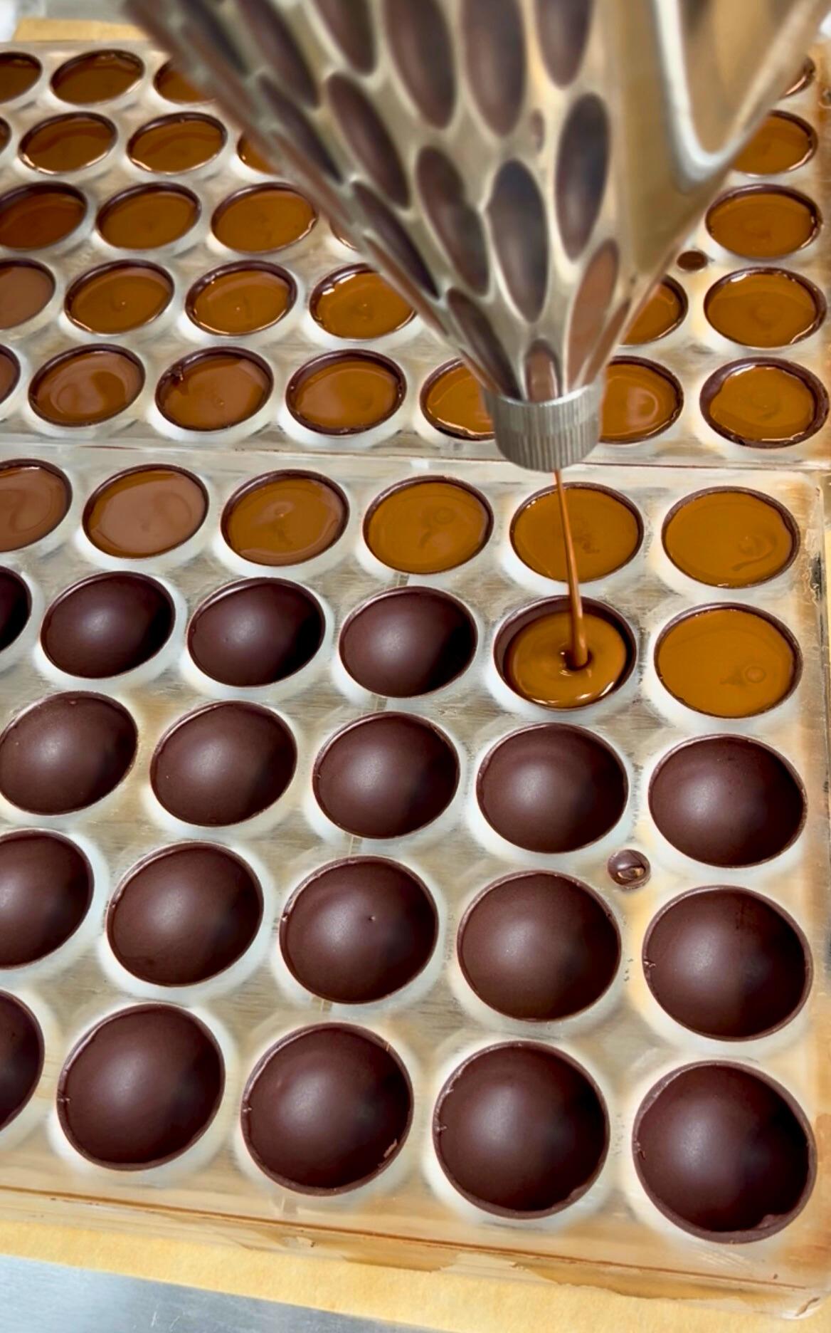 chocolate truffles being filled with ganache from a pastry funnel
