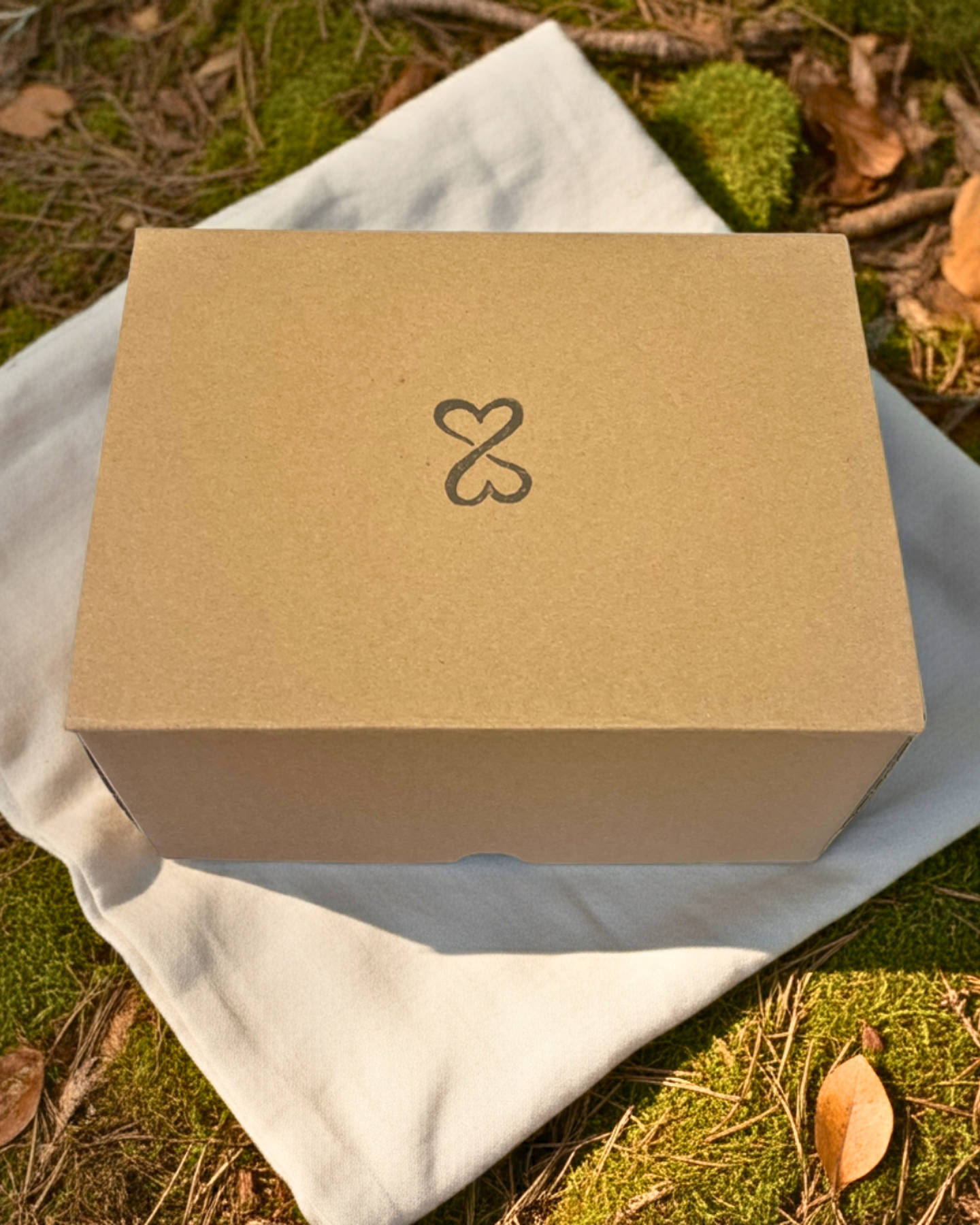 Brown kraft box with a double heart logo on a white cloth outdoors