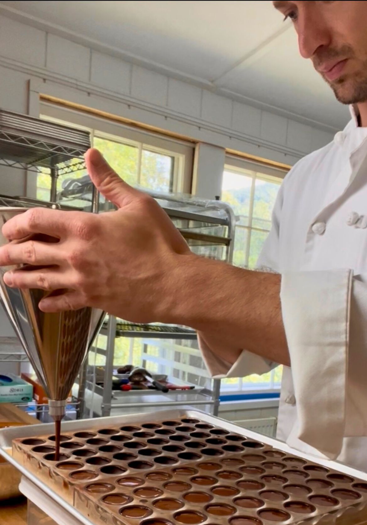 Person in a kitchen pouring chocolate into a mold using a pastry funnel