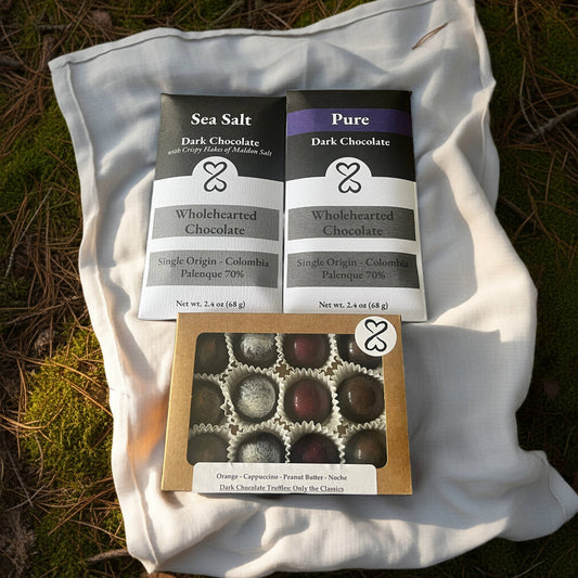 Two dark chocolate bars and a box of truffles on a white cloth with a natural background.