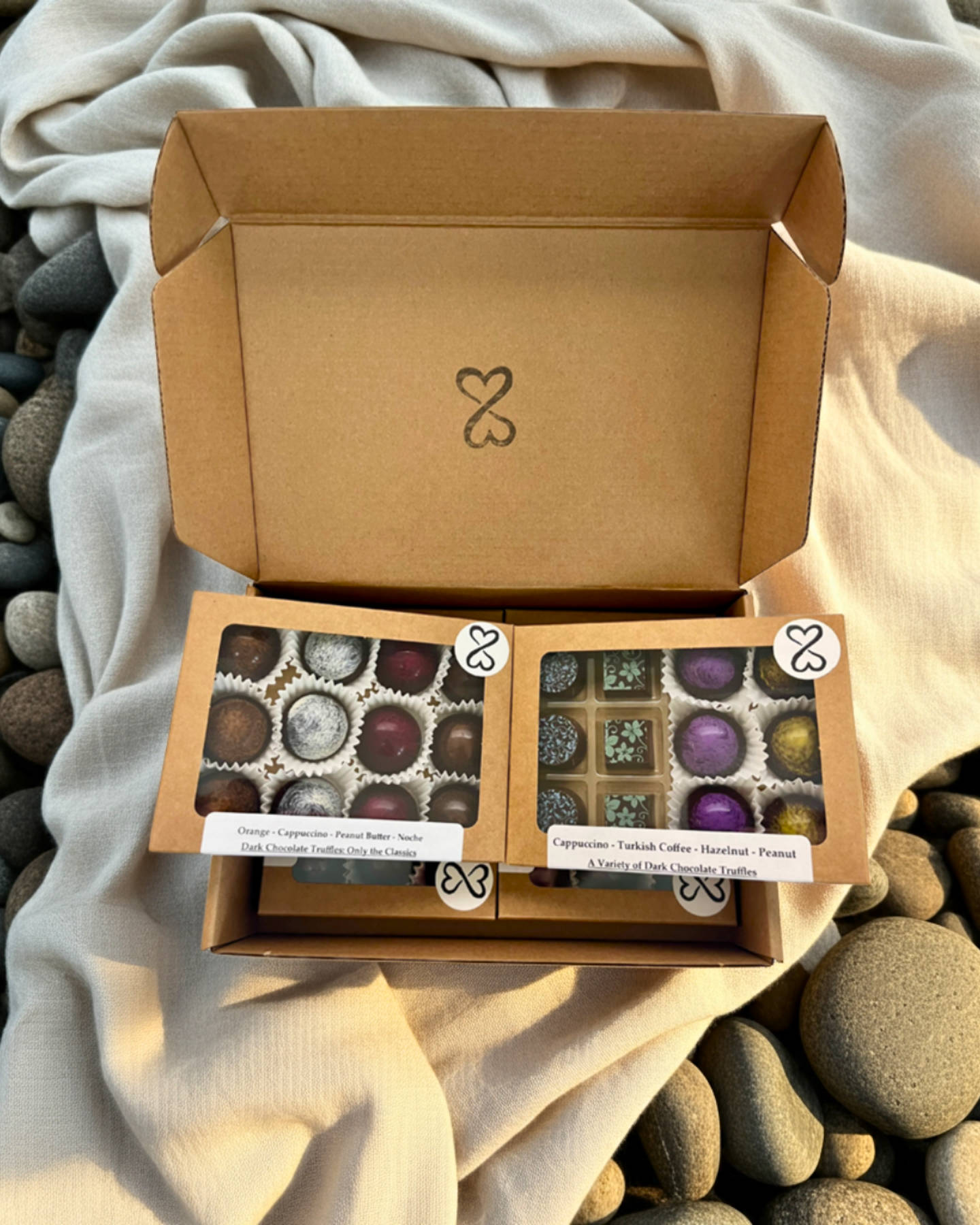 Open kraft box with multiple boxes of chocolate truffles on a textured fabric and stone background