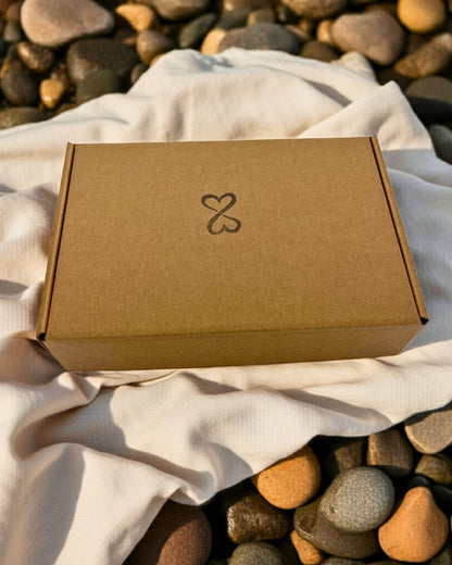 Brown kraft box with a double heart logo on a white fabric background with pebbles around
